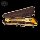 A Fender Stratocaster electric guitar in a sunburst finish, displayed inside an open vintage-style hard case with a tan textured exterior and dark brown velvet interior. The Fender logo is visible on the headstock (partially obscured) and the brand name 'FENDER' is printed on a small badge on the case's front panel.