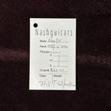 A white paper tag with handwritten details for a Nashguitars instrument, placed on a dark brown textured fabric background.