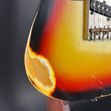Close-up of a sunburst electric guitar body showing a bright orange and yellow center fading to black around the edges, with part of the pickguard and strings visible.