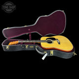 Acoustic guitar in an open case with 'Tone Shop' logo in the corner.