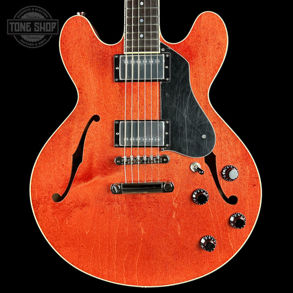 Orange electric guitar with a black pickguard on a black background, featuring 'Tone Shop' logo.