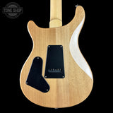 The back of an electric guitar with a natural wood finish, black pickguard, and a white maple binding, shown against a solid black background with a Tone Shop watermark in the top left corner.