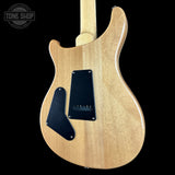 The back of an electric guitar with a natural maple wood finish, featuring black pickguard covers and a light-colored neck, shown against a solid black background.
