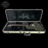 An electric guitar with a black body covered in gold polka dots, resting inside an open hard case with black velvet lining. The case has a cream-colored exterior and silver metal latches.