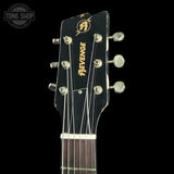 Close-up of the headstock of a black guitar with gold 'Revenge' branding and tuning pegs, shown against a black background with a Tone Shop watermark in the upper left.