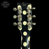 Close-up of the headstock of a black electric guitar with large cream-colored polka dots and six silver tuning pegs, shown against a black background.