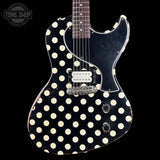 A classic electric guitar with a black body covered in a distressed cream polka-dot pattern, a black pickguard, and chrome hardware, shown against a solid black background.