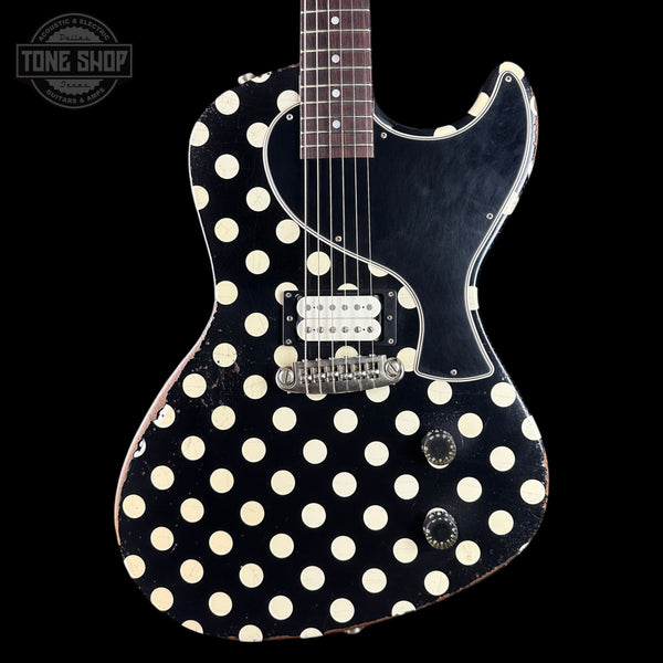 A classic electric guitar with a black body covered in a distressed cream polka-dot pattern, a black pickguard, and chrome hardware, shown against a solid black background.