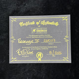 A gray Certificate of Authenticity card with yellow border lines and text, featuring the Rock N' Roll Relics Custom Shop logo and handwritten details for a 'Revenge Jr' model, placed on a black textured background.