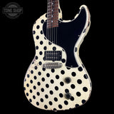 A vintage-style electric guitar with a cream-colored body covered in black polka dots, featuring a black pickguard and a dark fretboard, shown against a solid black background.