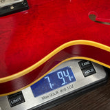 Red electric guitar being weighed on a digital scale with a display showing weight.
