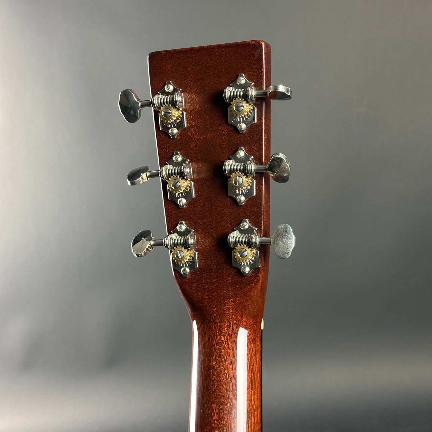 Close-up of a guitar headstock with tuning pegs on a gray background