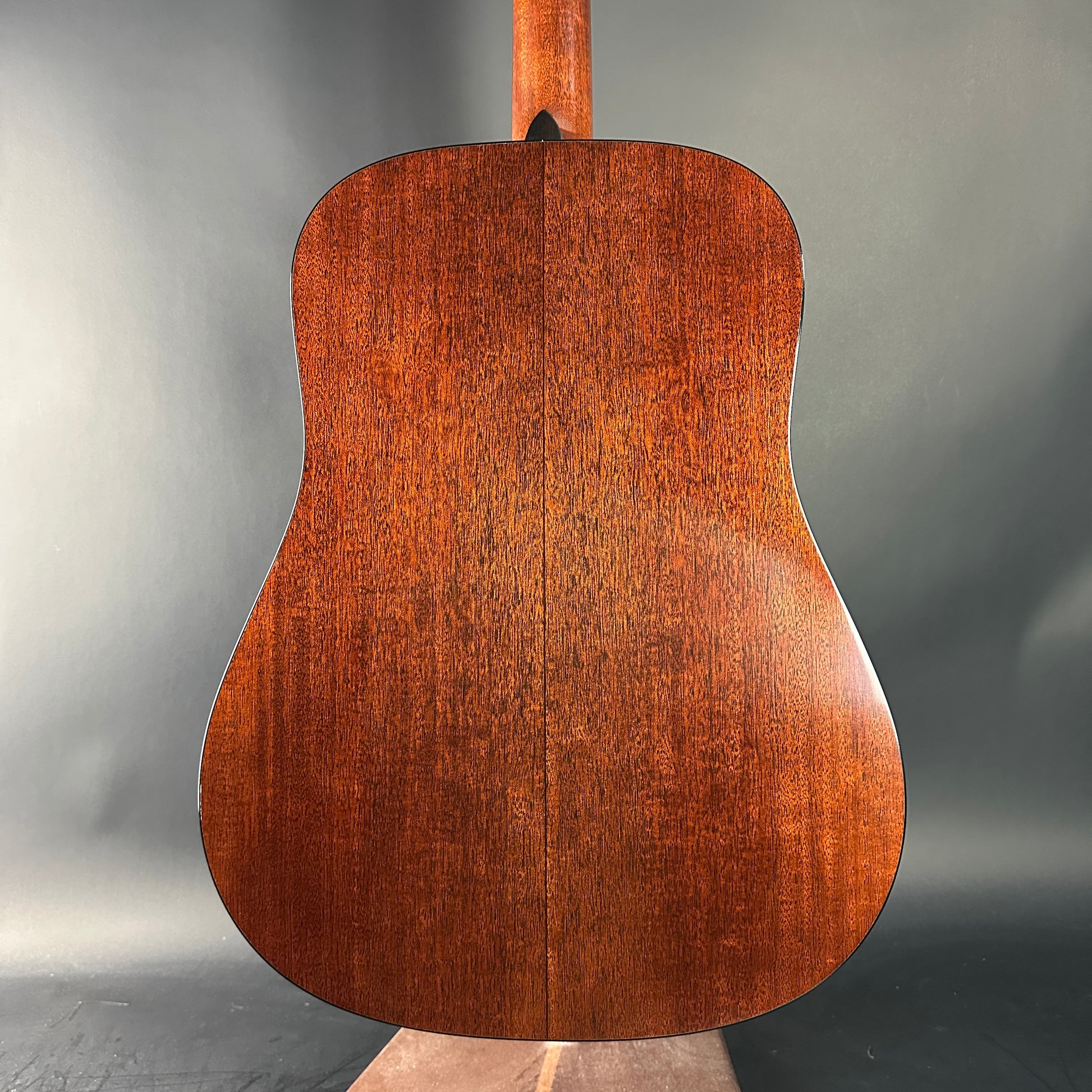 Back view of a wooden acoustic guitar on a gray background