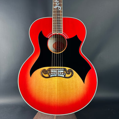 Red and orange acoustic guitar with a black pickguard on a dark background