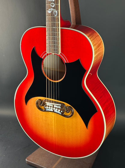 Red acoustic guitar with a black pickguard on a dark background