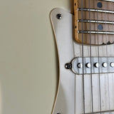 Close-up of a guitar body showing a cream-colored pickguard, silver hardware, and part of the natural wood fretboard with black fretboard dots.