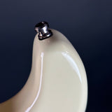 Close-up of a glossy cream-colored guitar body with a chrome metal tuning peg visible at the top, set against a dark navy background.