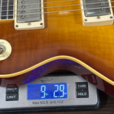 Guitar being weighed on a digital scale with a blue display.