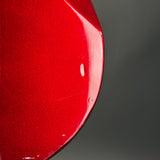 Close-up of a glossy red curved surface, likely part of a product, against a dark gray gradient background.