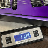 Purple electric guitar on a digital scale displaying weight.