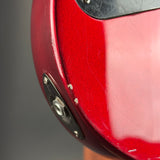 Close-up detail of a glossy red electric guitar body showing the edge contour, hardware mounting plates, and a small portion of the black pickguard against a dark gray background.