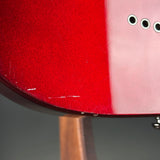 Close-up of a glossy red guitar body with visible wear, scratches, and a wooden stand below, photographed against a dark gray background.