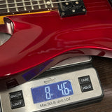A close-up of a glossy red electric guitar body resting on a digital scale displaying 8.46 oz, with the scale showing brand Weightmax.