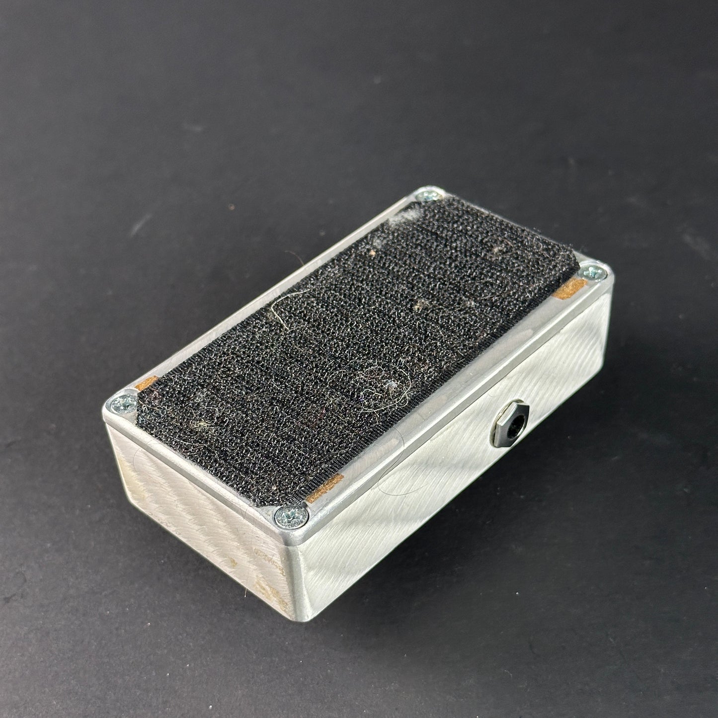 Metallic rectangular box with textured black top on a dark background