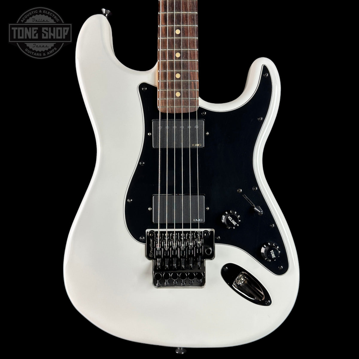 White electric guitar with a black pickguard on a black background, featuring the Tone Shop logo.