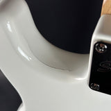 Close-up of a white guitar neck with a brand logo on a dark background
