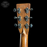 Close-up of the back of a guitar headstock made of warm brown wood with six ornate silver tuning pegs, shown against a solid black background. A Tone Shop watermark is visible in the top left corner.
