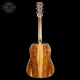 The back of an acoustic guitar with a rich, warm brown wood grain finish, shown against a solid black background with a Tone Shop watermark in the top left corner.