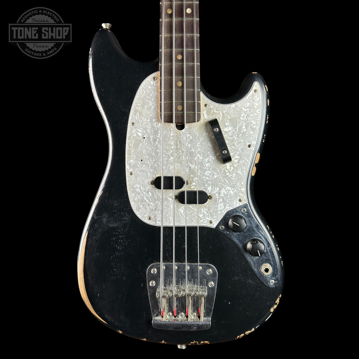 A vintage-style electric bass guitar with a black body, distressed finish, and a white marbled pickguard, shown against a solid black background. A Tone Shop logo is visible in the top-left corner.