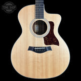 A Taylor acoustic guitar with a natural wood finish and a dark tortoiseshell pickguard, shown against a solid black background with a Tone Shop watermark in the top left corner.