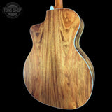 Close-up of the back of an acoustic guitar showing a rich wood grain finish, with a black background and a Tone Shop watermark in the top left corner.