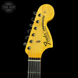 Close-up of a Fender Stratocaster electric guitar headstock in a bright yellow finish, showing six silver tuning pegs and the Fender logo, set against a solid black background.