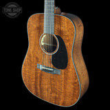 Acoustic guitar with a dark wood finish on a black background, featuring the Tone Shop logo.