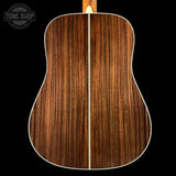 Back view of a wooden acoustic guitar with a visible brand logo in the corner.