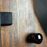 Close-up of a guitar with a black knob and tuning peg on a wooden surface.