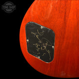 Close-up of the lower bout corner of an electric guitar body, showing a glossy reddish-orange wood finish and a black pickguard with gold hardware, photographed against a black background. A Tone Shop watermark is visible in the top-left corner.