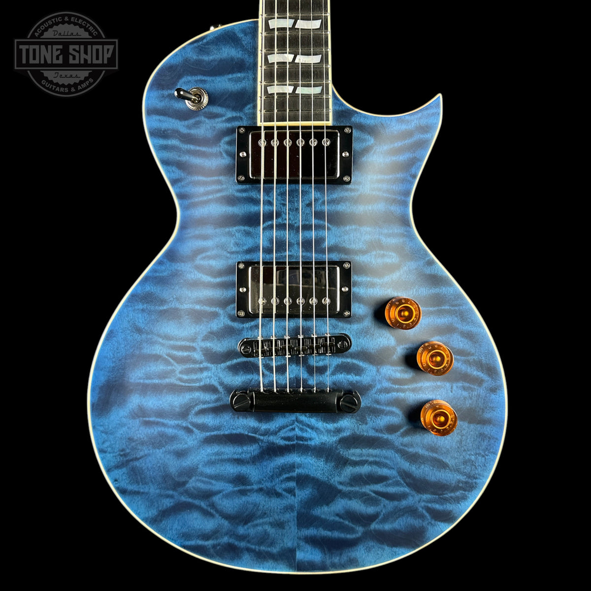 Blue electric guitar with a wavy pattern on a black background, featuring the Tone Shop logo.