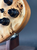 Close-up of a wooden guitar headstock with black tuning pegs on a blurred background