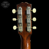 Close-up of a guitar headstock with tuning pegs on a black background, featuring the Tone Shop logo.