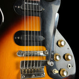 Close-up of a guitar with a black pickguard and gold hardware on a dark background
