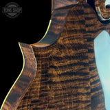 Close-up of a guitar's wooden neck and fretboard with 'Tone Shop' branding.
