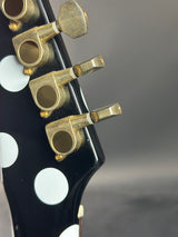Close-up of a guitar headstock with tuning pegs on a gray background