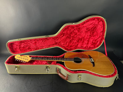 Acoustic guitar in an open case with red interior on a dark background
