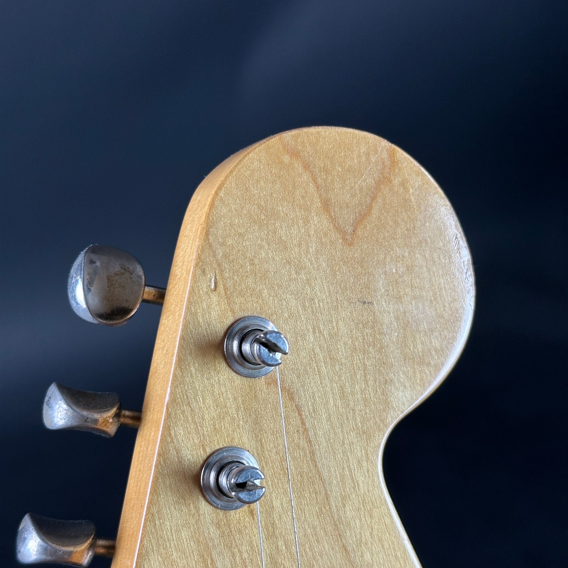 Close-up of a guitar headstock with tuning pegs on a dark background