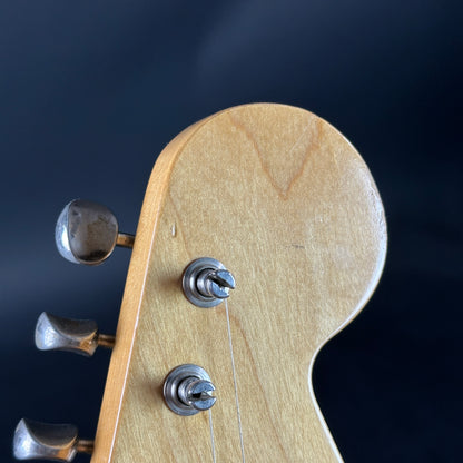 Close-up of a guitar headstock with tuning pegs on a dark background