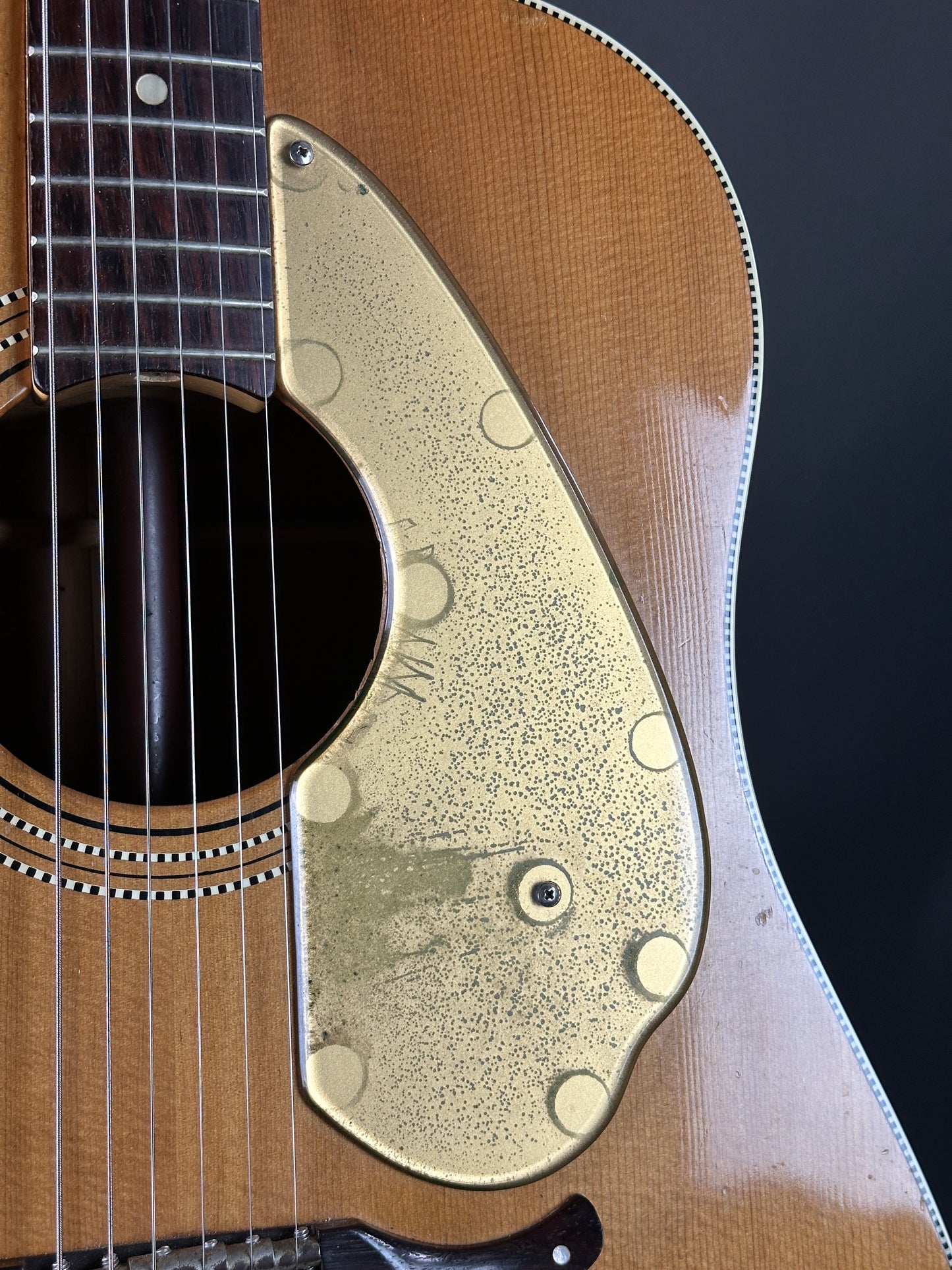 Close-up of a guitar's soundhole with a gold pickguard on a dark background